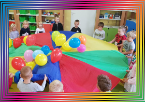 Dzieci trzymają chustę animacyjną, na której leżą kolorowe balony.